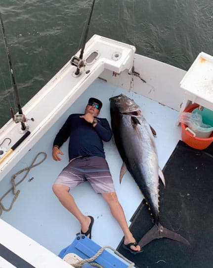 Man laying next to 6 foot tuna on boat deck